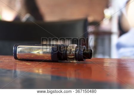 New Modern Shiny Electronic E-cigarette Box Laying On The Table In The Raw Club / Bar Environment Ma
