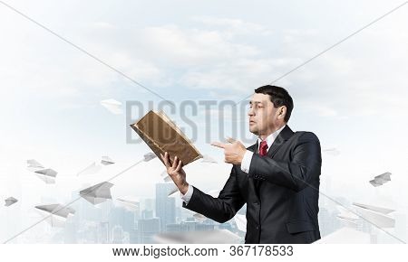 Senior Businessman Finger Pointing Into Open Book. Man In Business Suit And Tie Standing On Cityscap