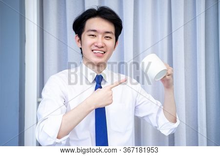 Asian Business Man Dringking Coffee Wearing Suit, Enjoying Watching Educational Webinar On Laptop Or