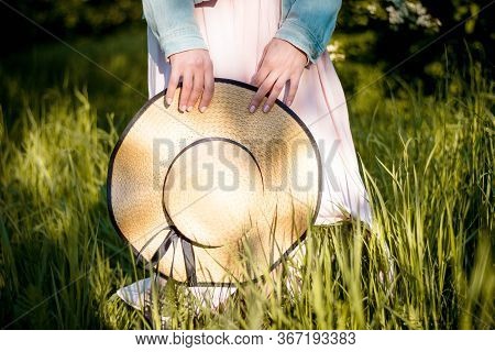 Straw Hat With Black Tape In The Habds Of A Woman In The Spring Garden