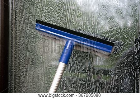 Cleaning Window Using A Squilgee To Wash Glass.