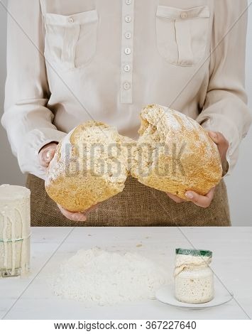 Baker Holds In His Hands A Freshly Baked Sourdough Bread, Broken In Half. Ingredients For Making Nat