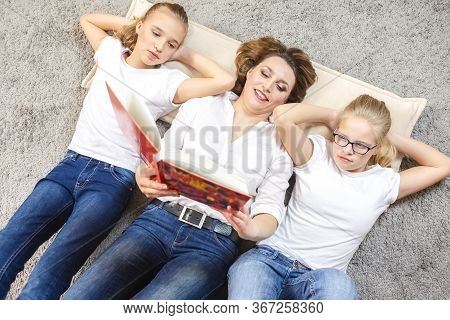 Family Ideas. Portrait Of Caucasian Mother Reading A Book Together With Her Female Twins Laying On F