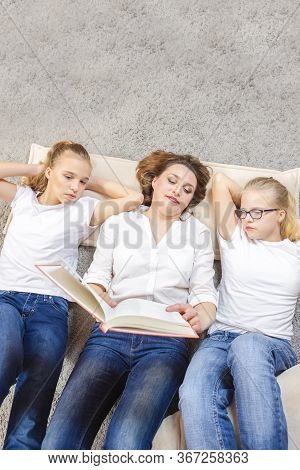 Family Ideas. Portrait Of Caucasian Mother Reading A Book Together With Her Female Twins Laying On F