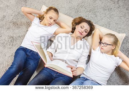 Family Concepts. Portrait Of Caucasian Mother Reading A Book Together With Her Female Twins Laying O