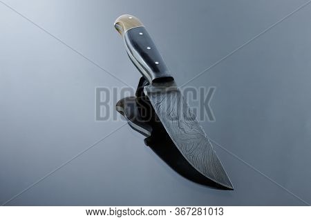 An All-metal, Middle Kitchen Knife Lies On A Mirror Surface, A Blade Made Of Multilayer Damask Steel