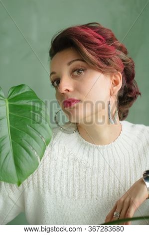 Portrait Of A Young Beautiful Woman With Perfect Smooth Skin With A Large Green Tropical Leaf. Fashi