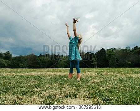 Little Girl Child Stand On Meadow With Hands Up To Sky In Hope. Freedom, Innocence And Adolescense C