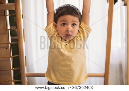 Cute Boy Hanging On Horizontal Bar While Exersicing In Home Gym