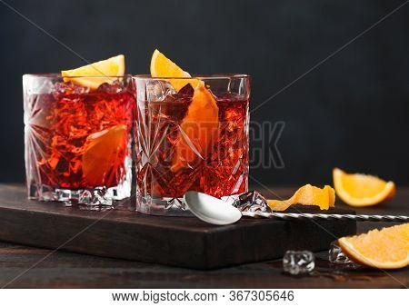 Negroni Cocktail In Crystal Glasses With Orange Slice And Fresh Raw Oranges On Chopping Board With S