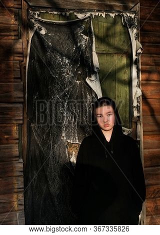 Pensive teenage girl in a black hoodie stands against the wall of an old abandoned building