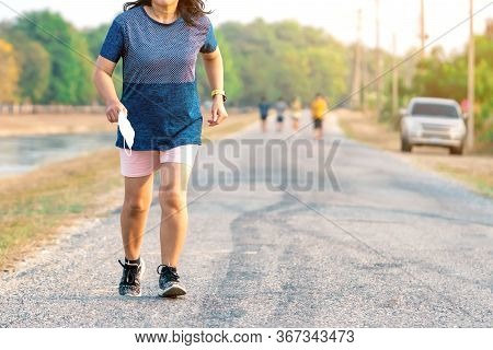 Sportive Woman Take Off Protective Mask While Jogging For Easier Breathing On Road Beside Irrigation