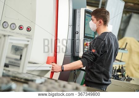 Industrial worker operating cnc machine in protective mask at metal machining industry