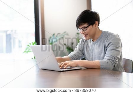 Young Asian Freelancer Man Sitting At A Table In A Cafe And Working On A Laptop. Happy Smile Man Wor