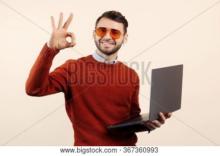 Smile Bearded Young Man In Casual Outfit With Notebook Or Computer Show Ok Gesture Over Beige Backgr