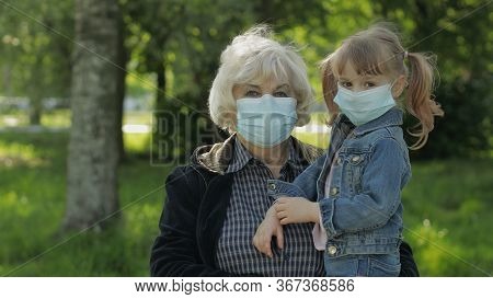 Old Grandmother With Granddaughter Together In Spring Park In Medical Masks. Coronavirus Covid-19 Pa