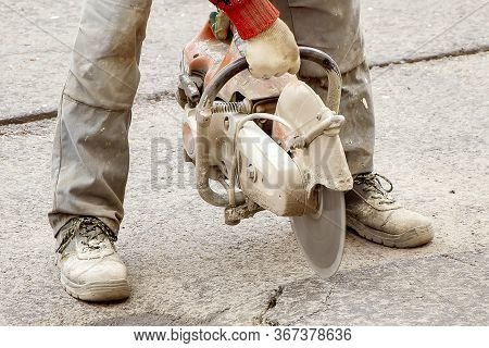 A Male Construction Worker Saws Asphalt With A Seamcutter, Dust Swirls From Under The Saw, Construct