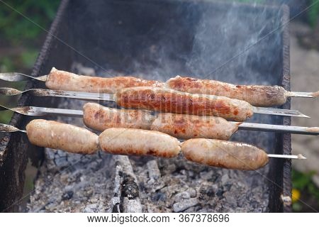 Close Up Of Toasted Sausages On Skewers. Succulent Kupaty Roasting On Chargrill. Concept Of Picnic O