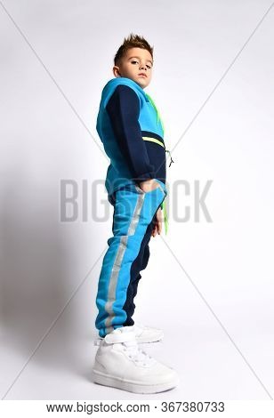Side View Shot Of A Little Schoolboy In A Bright Cotton Tracksuit Standing With Hands In Pockets Loo
