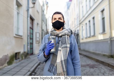 health, safety and pandemic concept - young woman wearing black face protective reusable barrier mask with tumbler or thermo cup on city street