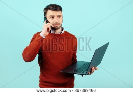 Astonished Bearded Young Man In Casual Outfit With Notebook Or Computer Talk On Smartphone Over Cyan