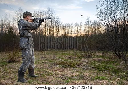 A Hunter Stands At Dusk In A Forest Clearing And Fires A Shotgun At A Low-flying Male Woodcock, Whic