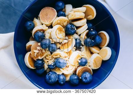Close- Up Of Mini Pancake Cereal, Mini Pancakes In A Dark Blue Bowl With Maple Sirup Honey With Blue