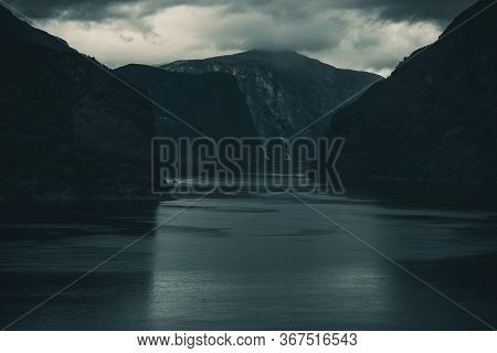 View Of Narrow Water Passage Between Steep Norwegian Cliffs At Dask With Cloudy Sky And Boats In Riv