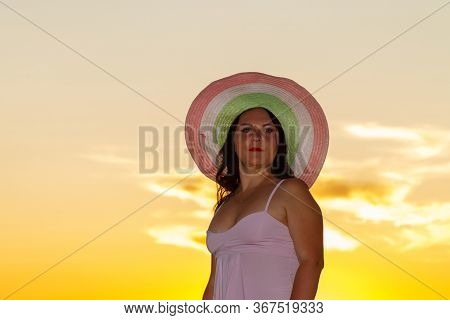 Woman In A White Dress And Hat On A Background Of A Sunset Sky.