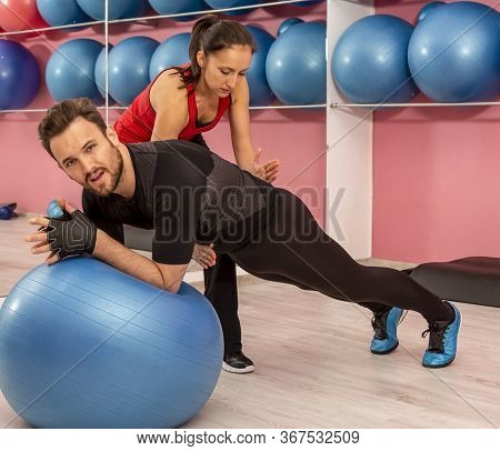 Young Man Helped By His Coach Doing Stretching Exrcises With A Fitness Ball In A Gym.