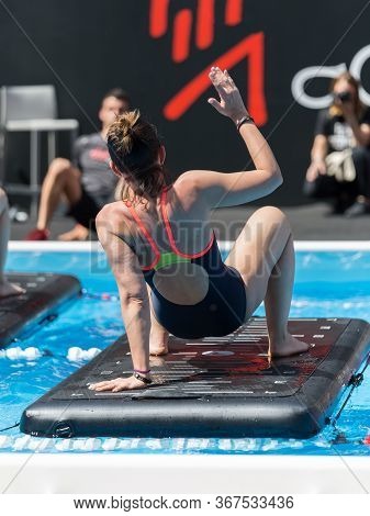Girl Doing Exercises On Floating Fitness Mat In An Outdoor Swimming Pool.