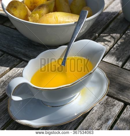 Melted Butter In A White Sauce Boat And Boiled Potatoes In A Bowl On A Wooden Garden Table, Selected