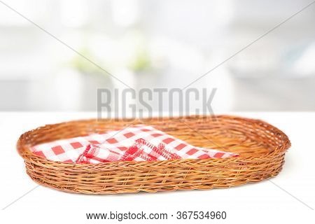 Oval-shaped Wicker Basket And Checkered Cotton Napkin Inside On A White Table Table