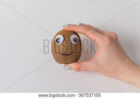 Female Hand Holding Cute Kiwi With Googly Eyes And Painted Smile. White Background. Kiwi Character.