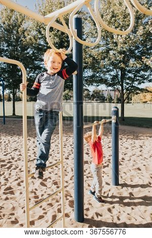 Young Caucasian Boys Friends Hanging On Monkey Bars And Pull-up Bars In Park On Playground. Summer O