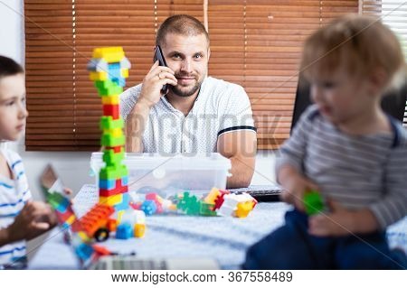 A Young Man Dad Talking On The Phone And Trying To Work At A Computer At A Remote Work During The Pe