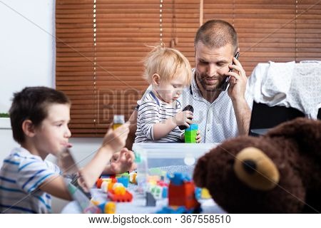 A Young Man Dad Talking On The Phone And Trying To Work At A Computer At A Remote Work During The Pe