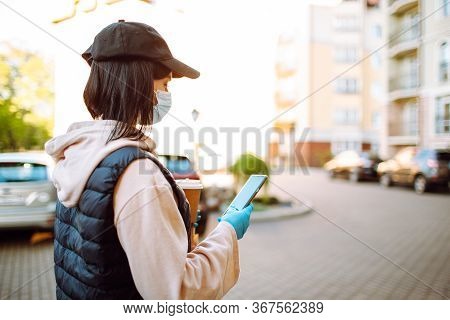 Delivery Woman In Protective Face Mask And Gloves With A Bag Of Food And Coffee Checking Addres With