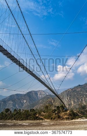 A Big Suspension Pedestrian Bridge Crossing A Rough Mountain River In The Himalayas. View From Under