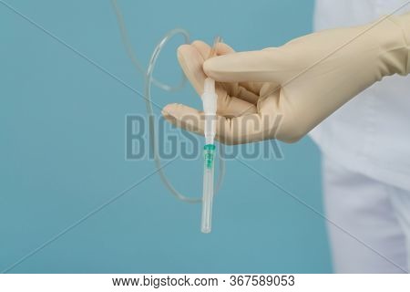 Doctor Holds A Catheter In His Hands On A Blue Background