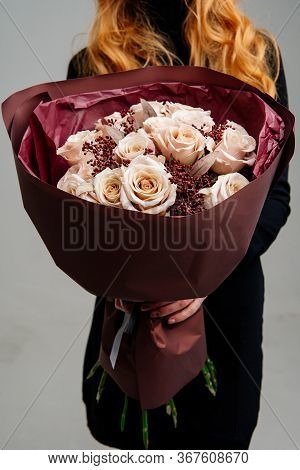Bouquet Of Flowers In Burgundy Package In The Hands Of Red-haired Girl Florist On Light Background. 