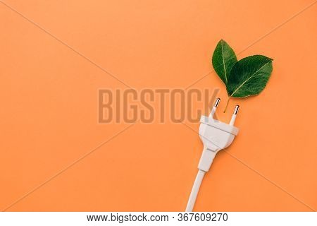 Creative Top View Flat Lay Of Electrical Plug, Fresh Green Leaves With Copy Space On Orange Backgrou