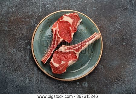 Two Raw Marbled Tomahawk Meat Steaks On Plate, Concrete Background. Premium Beef Steak On Bone Prepa
