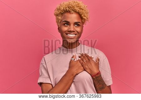 Smiling Cheerful Dark Skinned Young Female Keeps Palms On Heart, Expresses Appreciation, Pleasure An