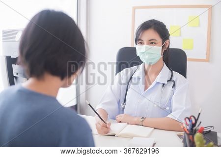 An Asian female doctor wearing a surgical mask is inquiring about the condition of the patient.