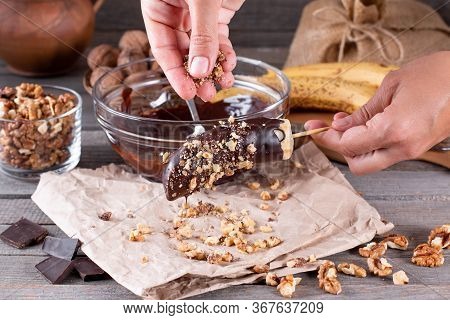 Woman Hands Sprinkle Nuts On A Frozen Banana. Frozen Chocolate Covered Bananas On A Stick