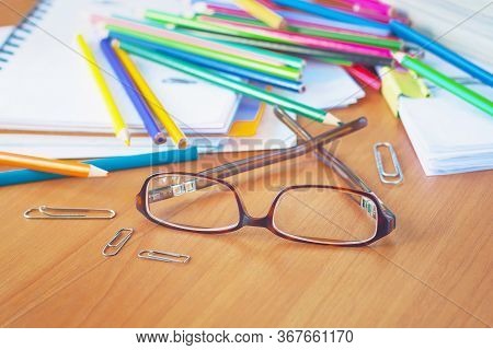 Glasses On The Background Of Colored Pencils And Paper. The Clutter On The Desktop.