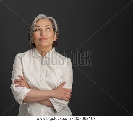 Creative Mature Woman Looking Upward Thoughtfully With Her Arms Crossed. Charming Silver-haired Woma