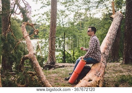 Man Eating An Apple On Hiking Trip In Forest. Hiker Taking Break While Trekking In Wilderness. Male 
