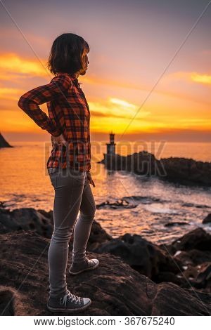 A Young Woman In A Plaid Shirt At The Sunset Of The Pasajes San Juan Lighthouse, Near San Sebastian,
